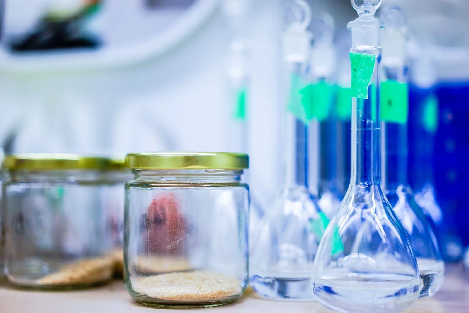 Laboratory volumetric flasks holding blue solution alongside sample jars on a life-sciences lab bench.